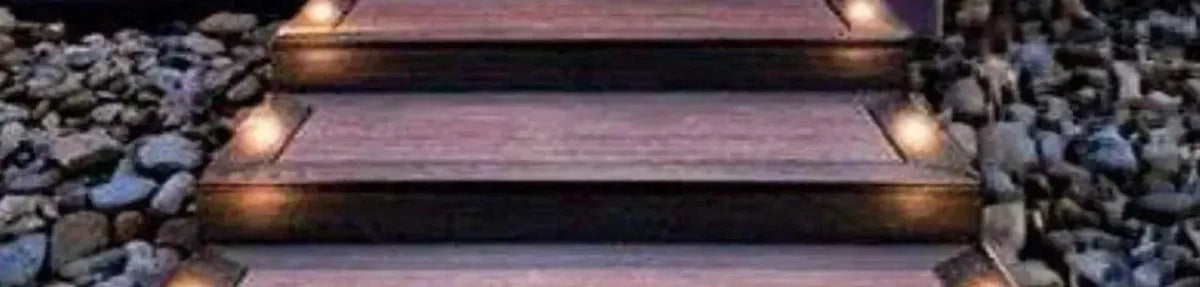 Round solar deck lights mounted on the edges of dark timber stairs surrounded by decorative garden pebbles