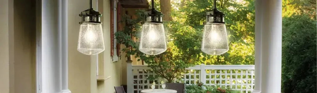 Three black metal pendants with seeded glass shades hanging on a covered outdoor patio overlooking a garden