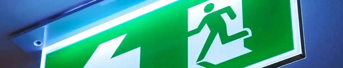 Illuminated green and white rectangular exit sign with a running person icon mounted on a ceiling surface