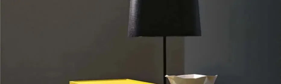 Minimalist black table lamp with a textured drum shade on a slim stand beside a bright yellow side table