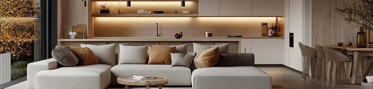Warm LED strip lighting illuminates a modern kitchen with timber accents and a neutral fabric sofa in an open plan space
