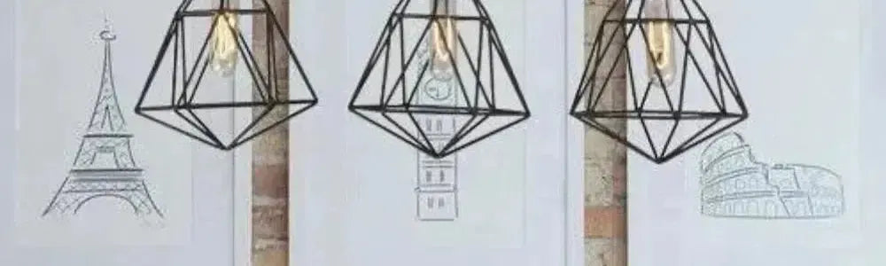 Three black geometric cage pendant lights hanging in front of framed travel sketches against a rustic brick wall