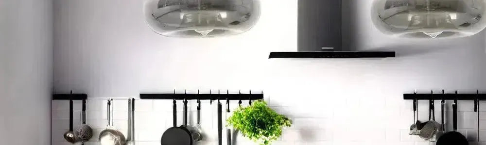 Round smoked glass pendant lights suspended over a modern kitchen bench with white subway tiles and black utensil rails