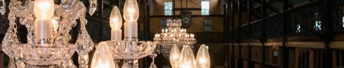 Ornate crystal chandeliers with candle style globes suspended in a grand historic hall with timber balconies