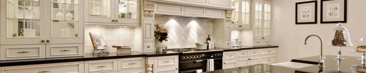Cream cabinetry with ornate corbels and glass doors featuring a black stone benchtop in a classic kitchen setting