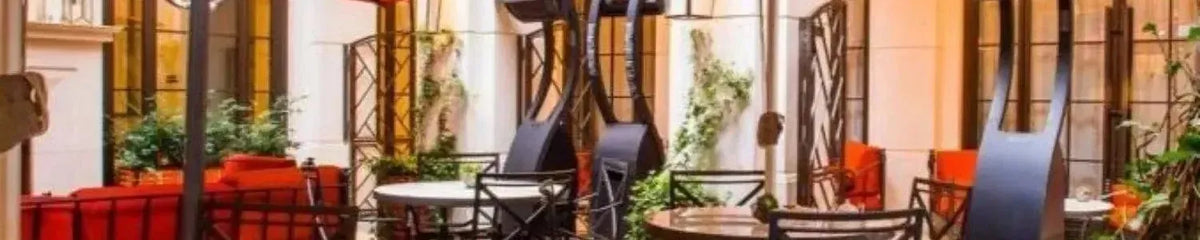 Black curved outdoor gas heaters standing on a paved patio with red seating and lush greenery