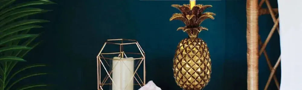 Antique gold pineapple table lamp with a white shade set against a dark teal wall with rattan furniture