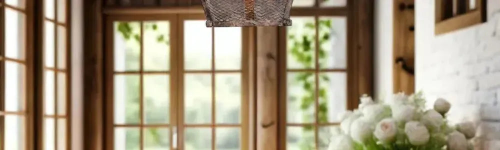 Rustic bronze wire cage pendant light hanging above a dining table in a sunlit room with timber window frames