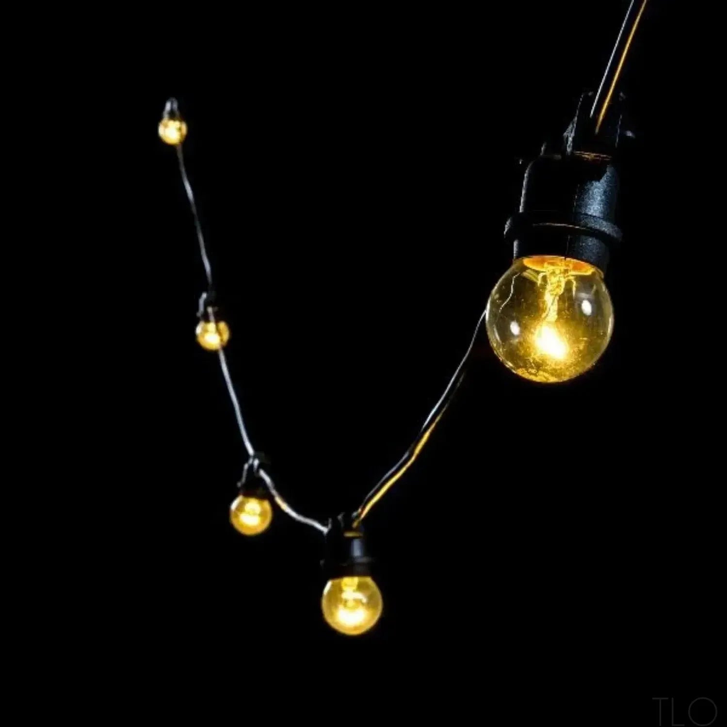 Outdoor festoon lights with warm glowing filament bulbs on a black cable against a dark background.