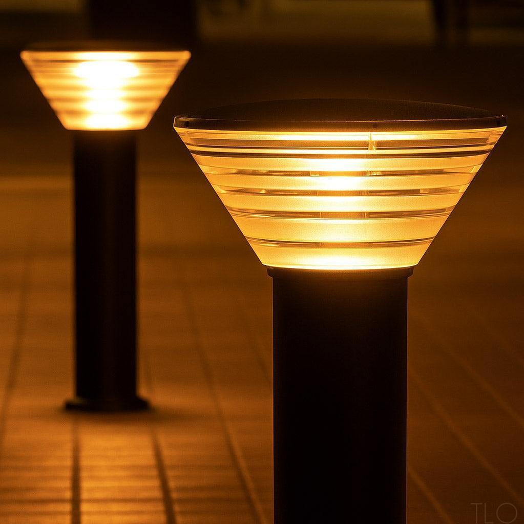 Two modern black outdoor bollard lights with warm yellow glow and horizontal frosted diffusers.