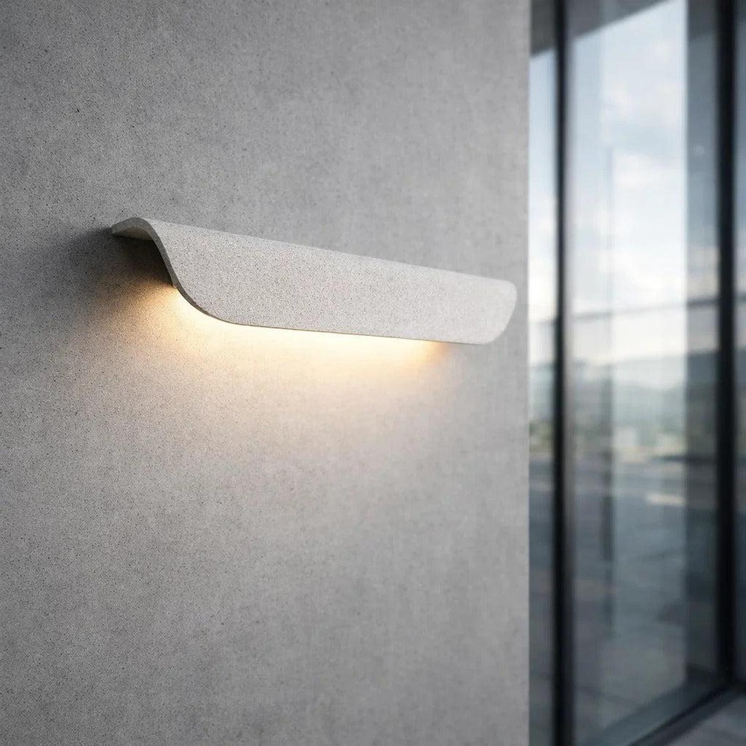 Long curved white cement outdoor wall light mounted on a concrete wall, casting a soft downward glow.