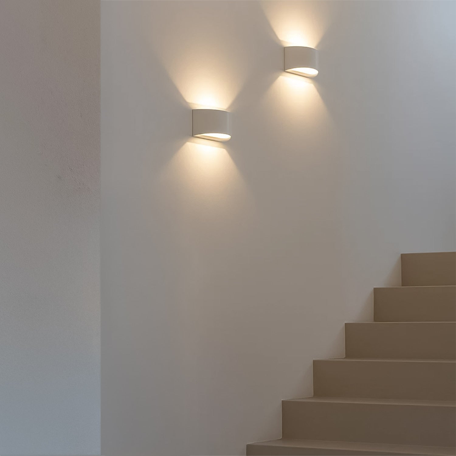 Two white plaster Numa up/down wall lights illuminating a modern staircase with warm, sculptural light.