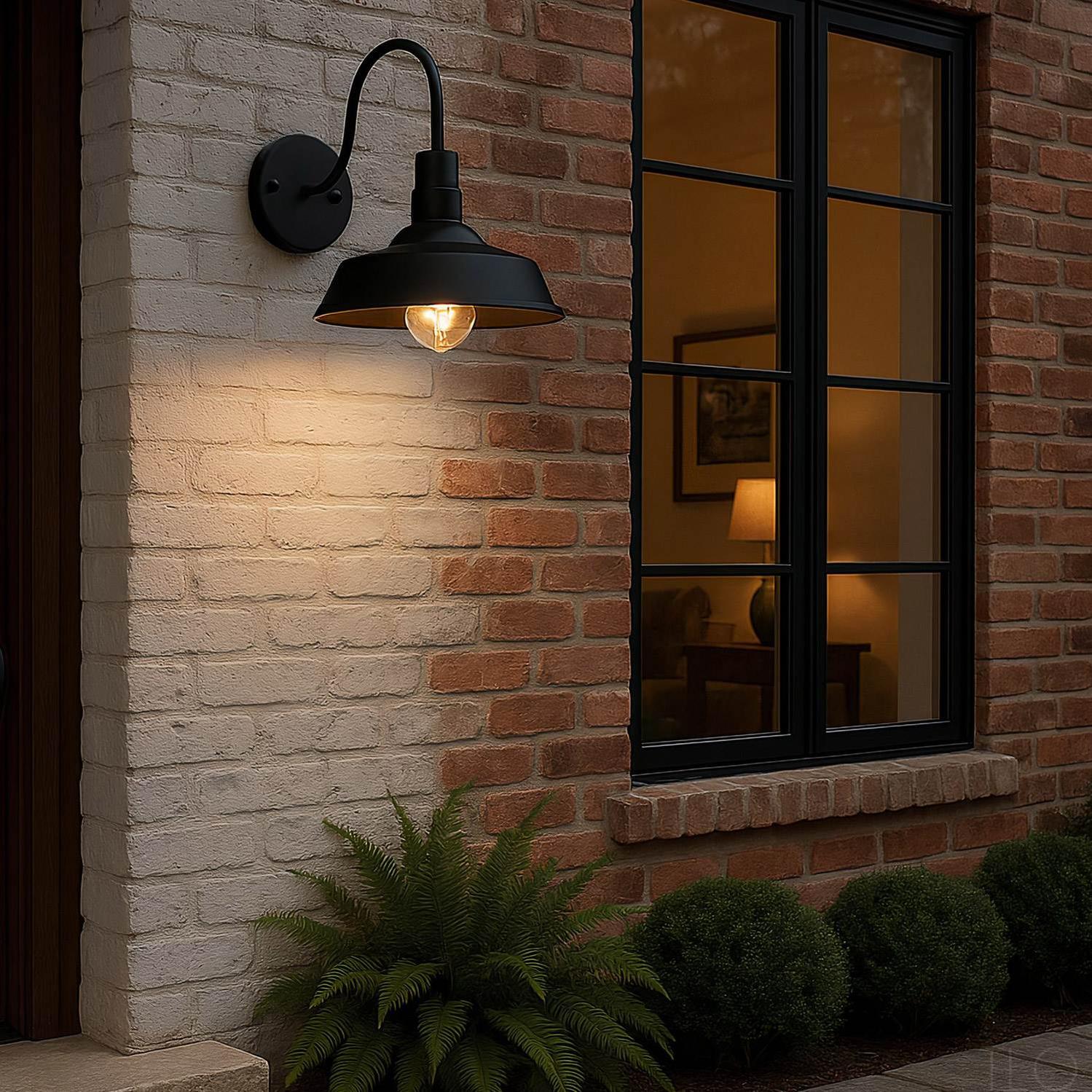 Black barn-style outdoor wall light with a curved arm, mounted on a brick exterior wall with a warm glowing E27 bulb.