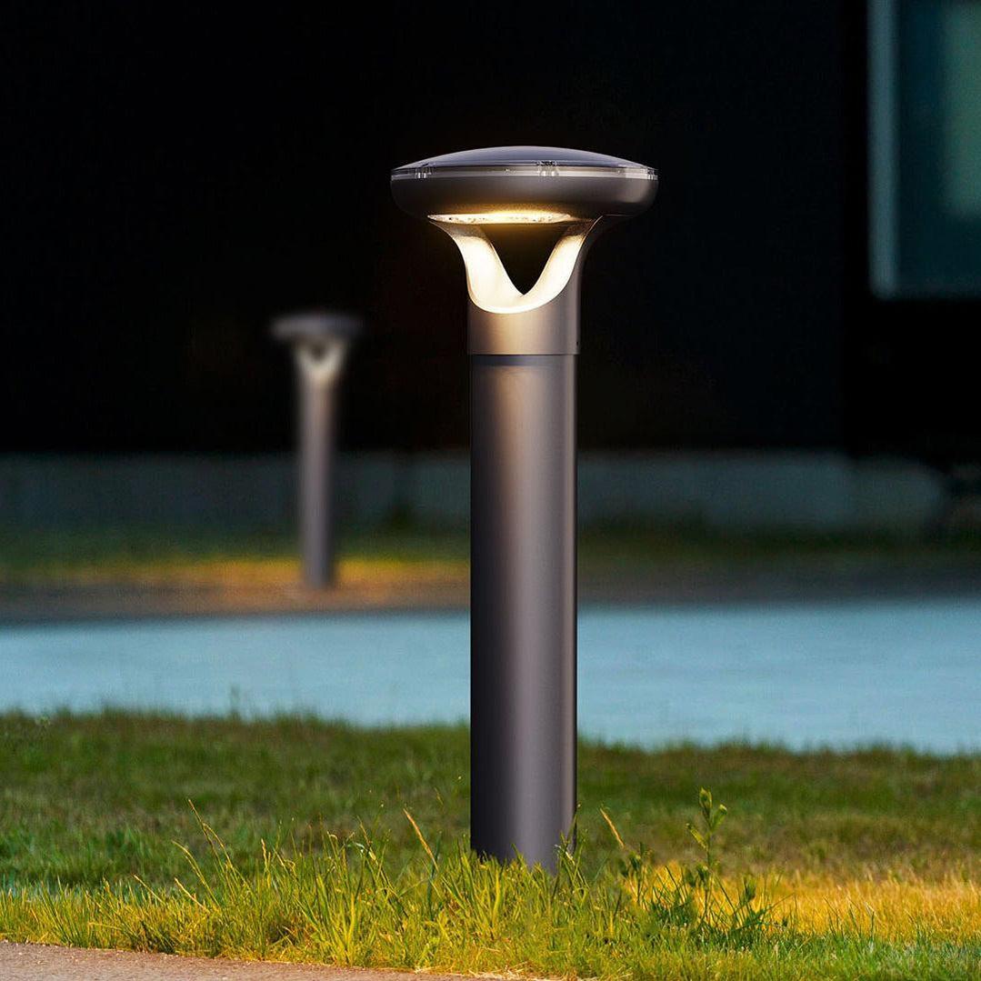 Outdoor solar bollard light in dark gray, modern design, illuminating grass and pathway.
