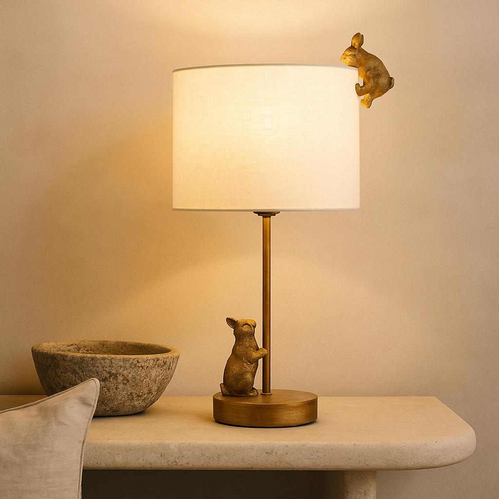Quinn gold iron table lamp featuring two playful rabbit figures and a white fabric shade on a stone console table.