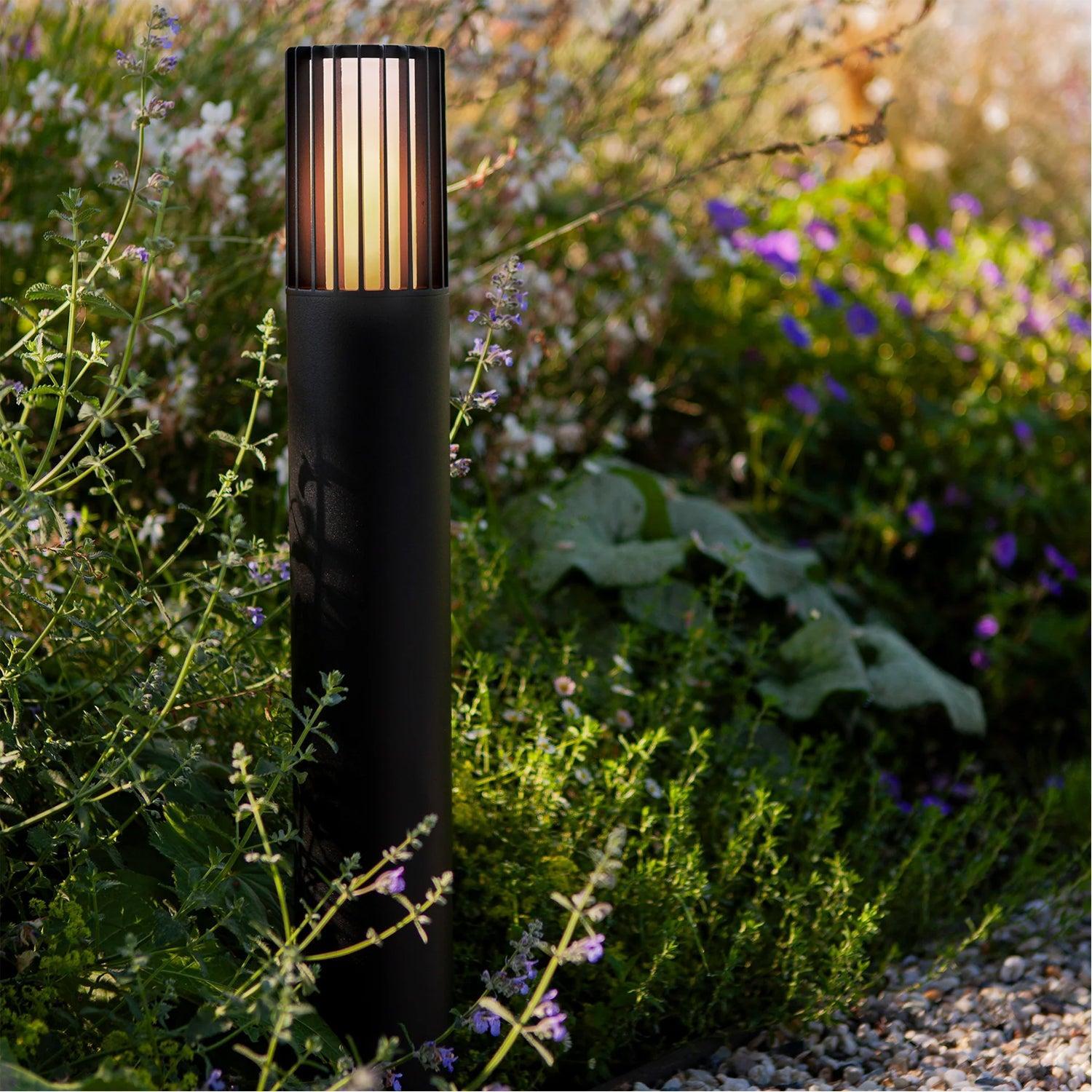 Outdoor black bollard light with a bronze slatted top, illuminating a garden path.