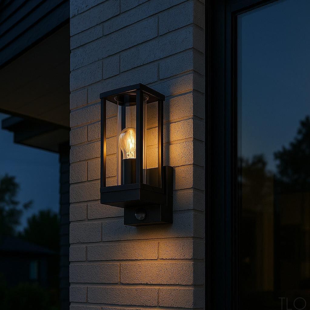 Black die-cast aluminium modern coach wall light with motion sensor and warm Edison bulb on a brick exterior wall.