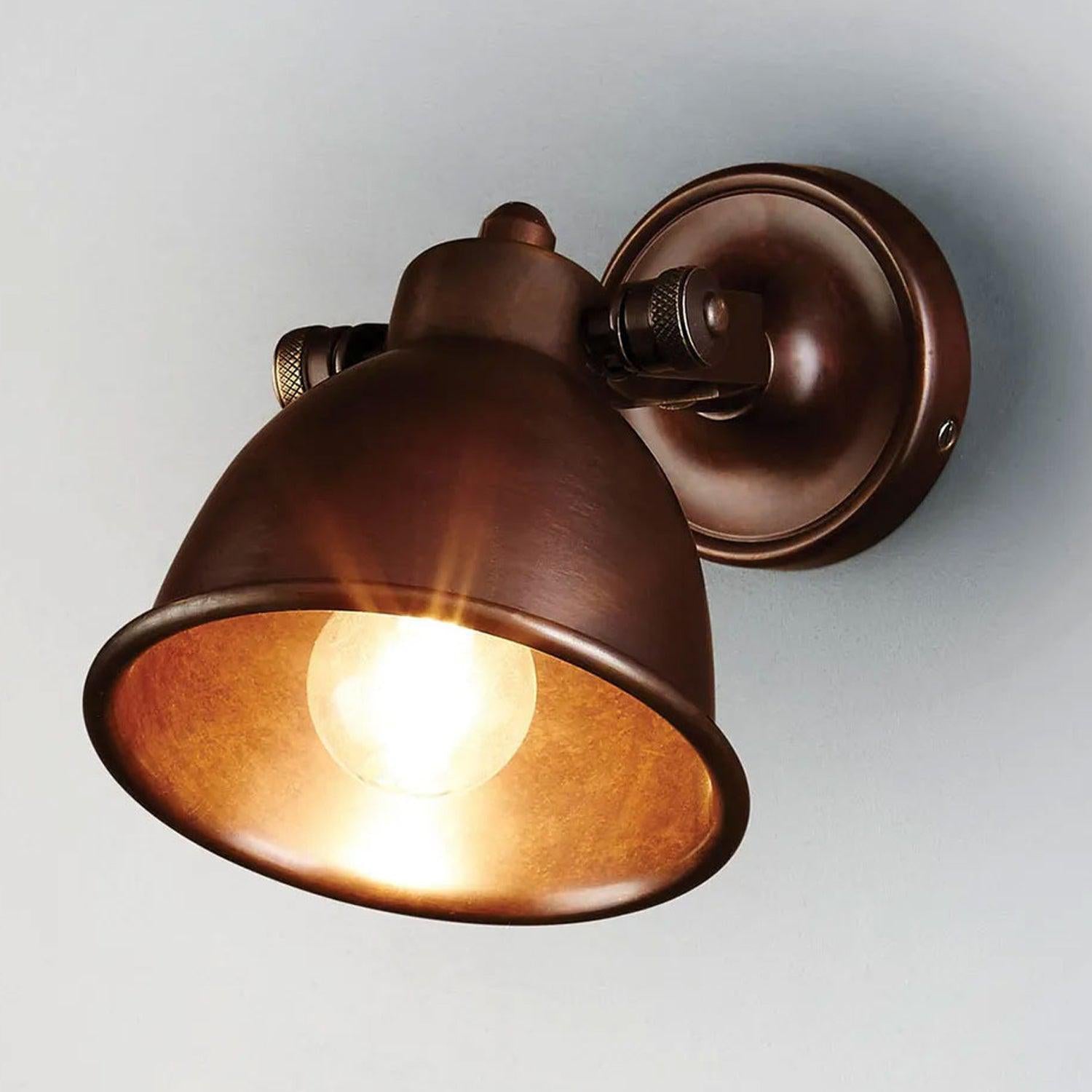 Phoenix wall lamp in antique dark brass with a dome-shaped shade and adjustable mounting bracket.